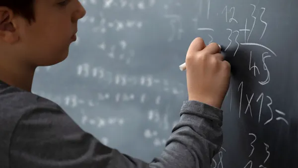 A student works on a math problem on a chalkboard in a classroom.