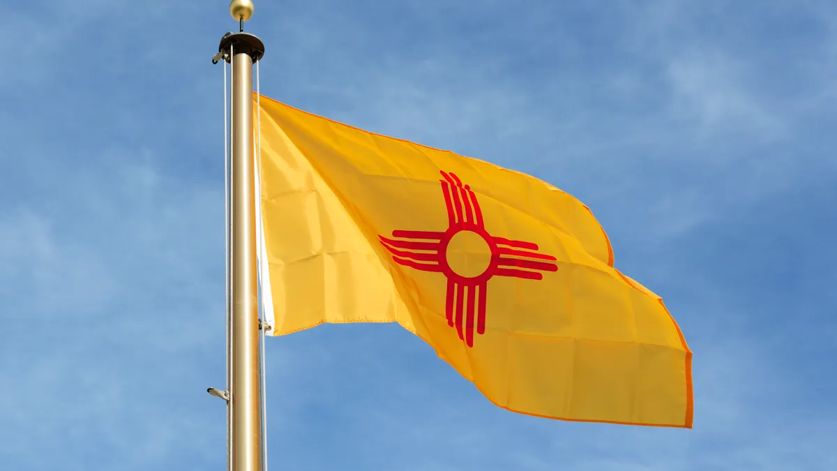 The New Mexico state flag waves in the wind with a clear sky behind it.