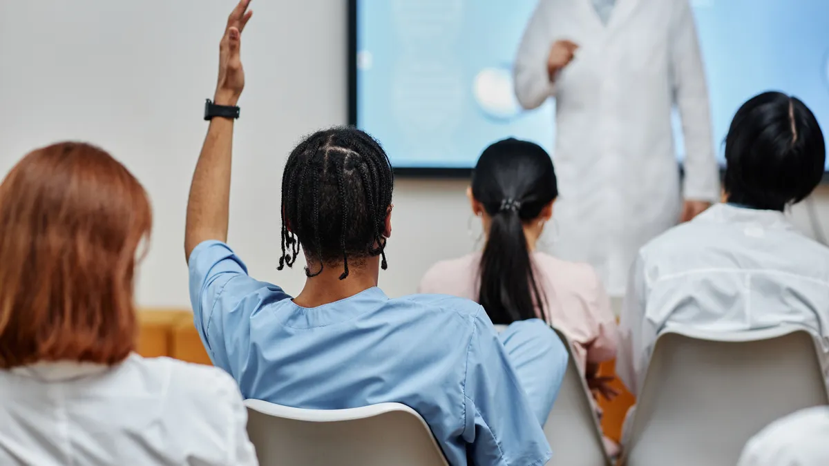 A person in a blue shirt raises their hand during a medical training seminar.