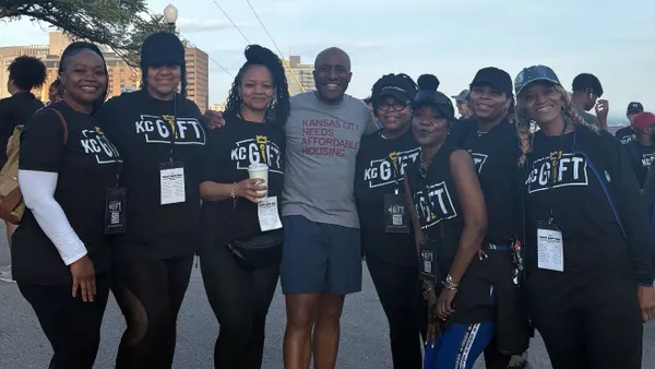 A person wearing a t-shirt that says "Build Affordable Housing" standing with group of people wearing black pants and black t-shirts.