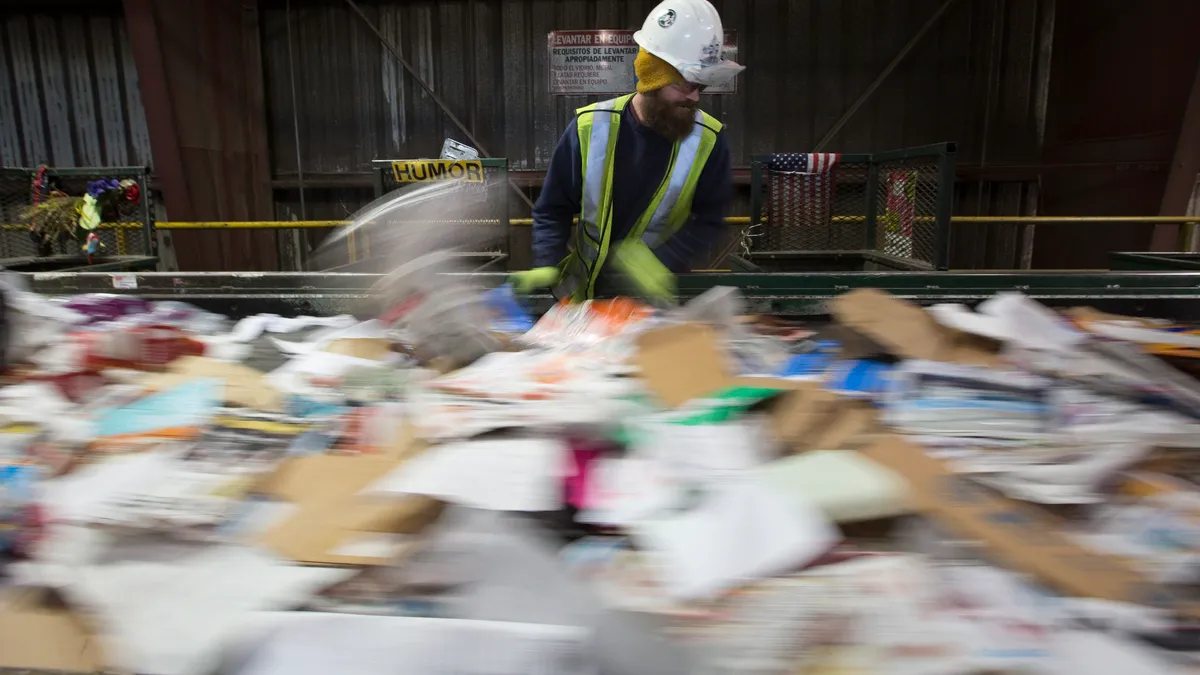 Person in hard hat and safety vest stands over fast-moving conveyor belt with recyclables in Oregon