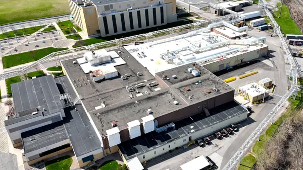 Aerial view of a large pharma manufacturing facility with two large buildings in the center surrounded by small building, parking lots and grass