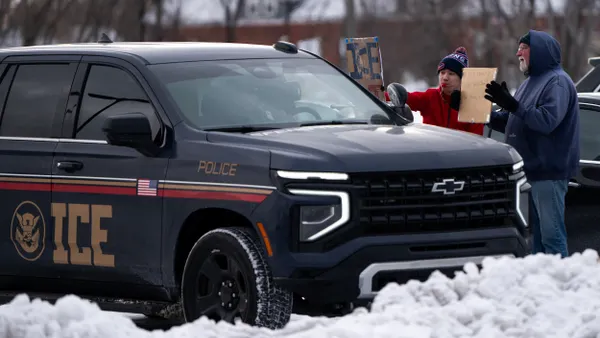 Two people hold cardboard signs up to a black SUV with "ICE" and "Police" written on the side.