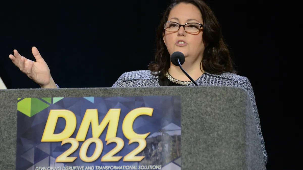 Woman glasses speaking at the podium with heavy lights on her.