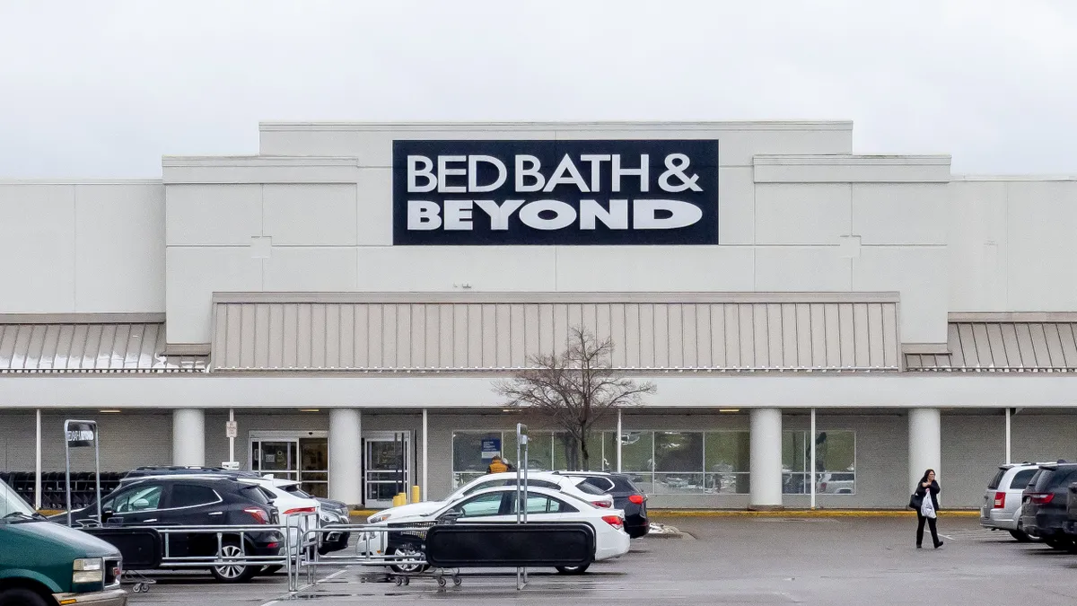 Cars are parked in front of a white building, against a white sky, with a dark blue banner that says "Bed Bath & Beyond" in white capital letters.