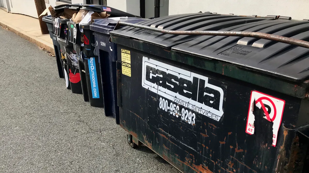 A dumpster with the Casella logo sits in an alley