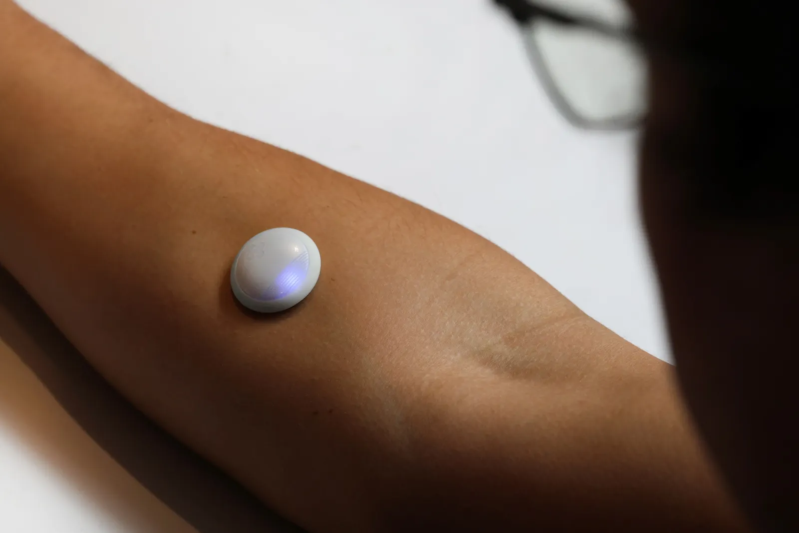 A person wears a small, white round sensor on their forearm.