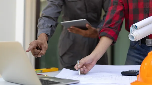 An engineer and business owner look at tables and computers to help with work.