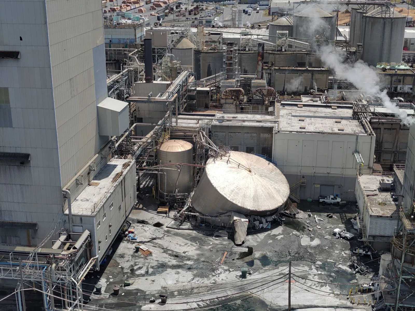 A collapsed tank amid other equipment at the exterior of an industrial site.