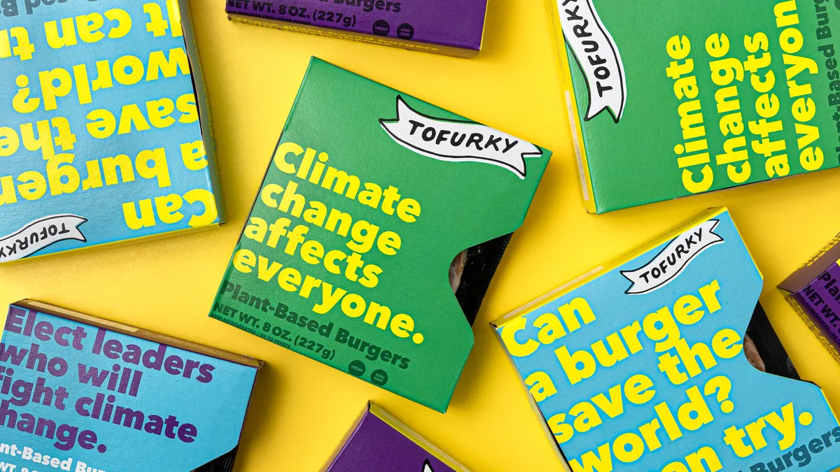 Several colorful packages of Tofurky's plant-based burgers with messages about climate change loosely tiled on a yellow surface
