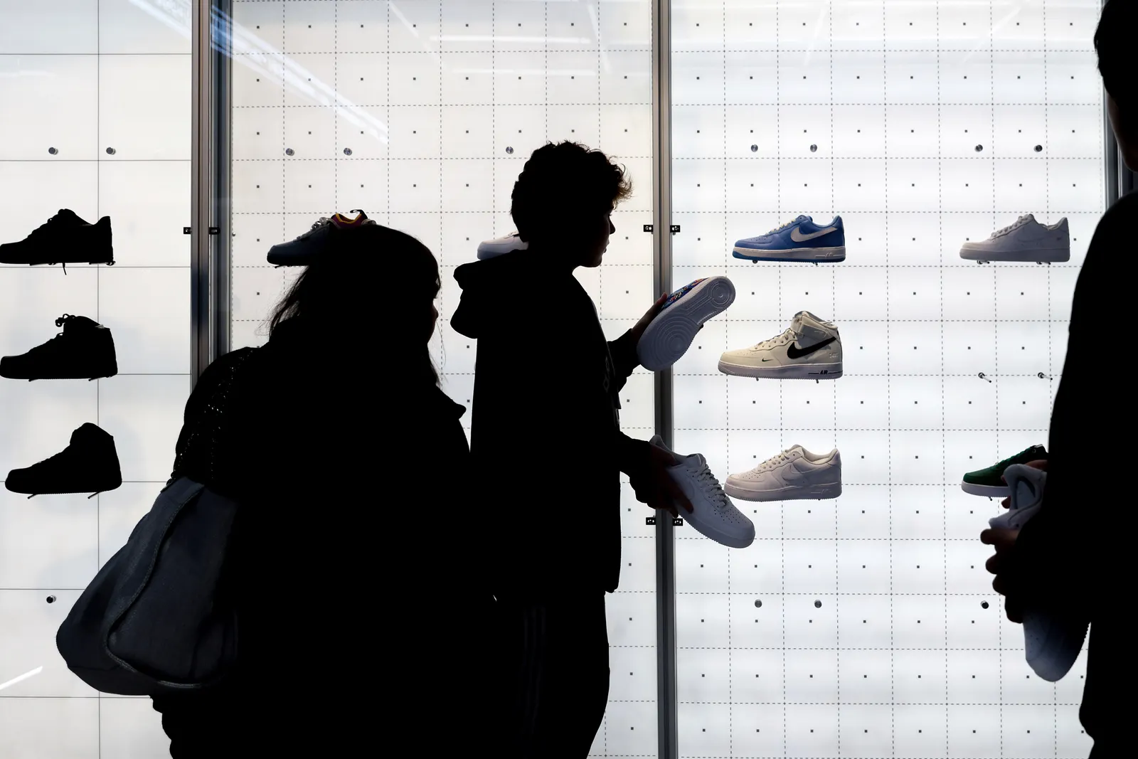 A silhouetted group of people holding Nike shoes in front of a white cubed shoe display.