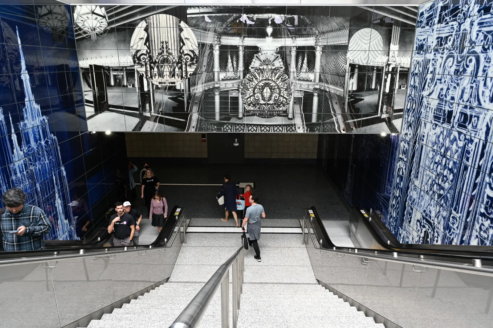 Several poeple on stairs and escalators leading down with artwork overhead and alongside.
