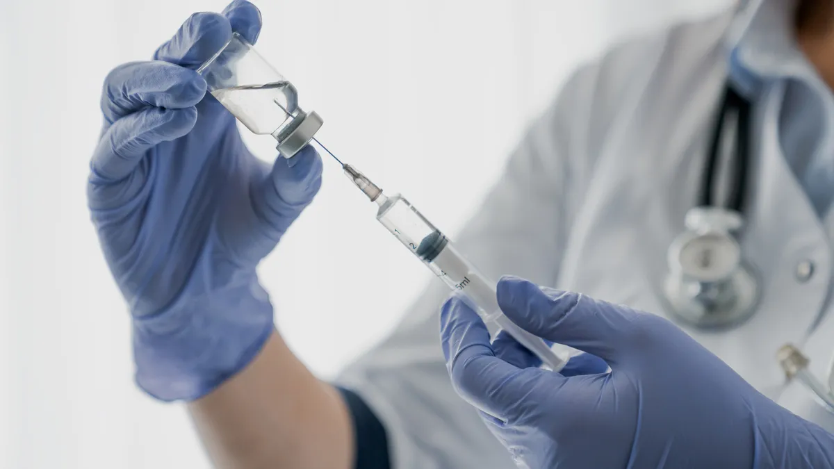 Medication nurse wearing protective gloves get a needle ready for an injection.