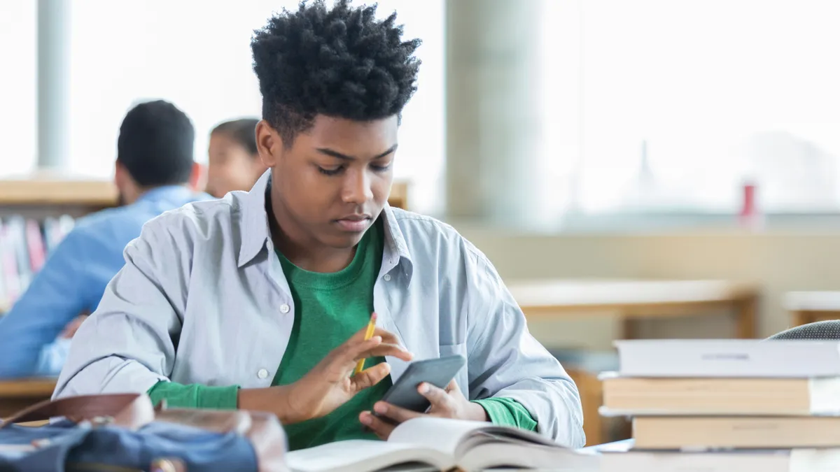 A high school student holds a calculator while completing an assignment in class.