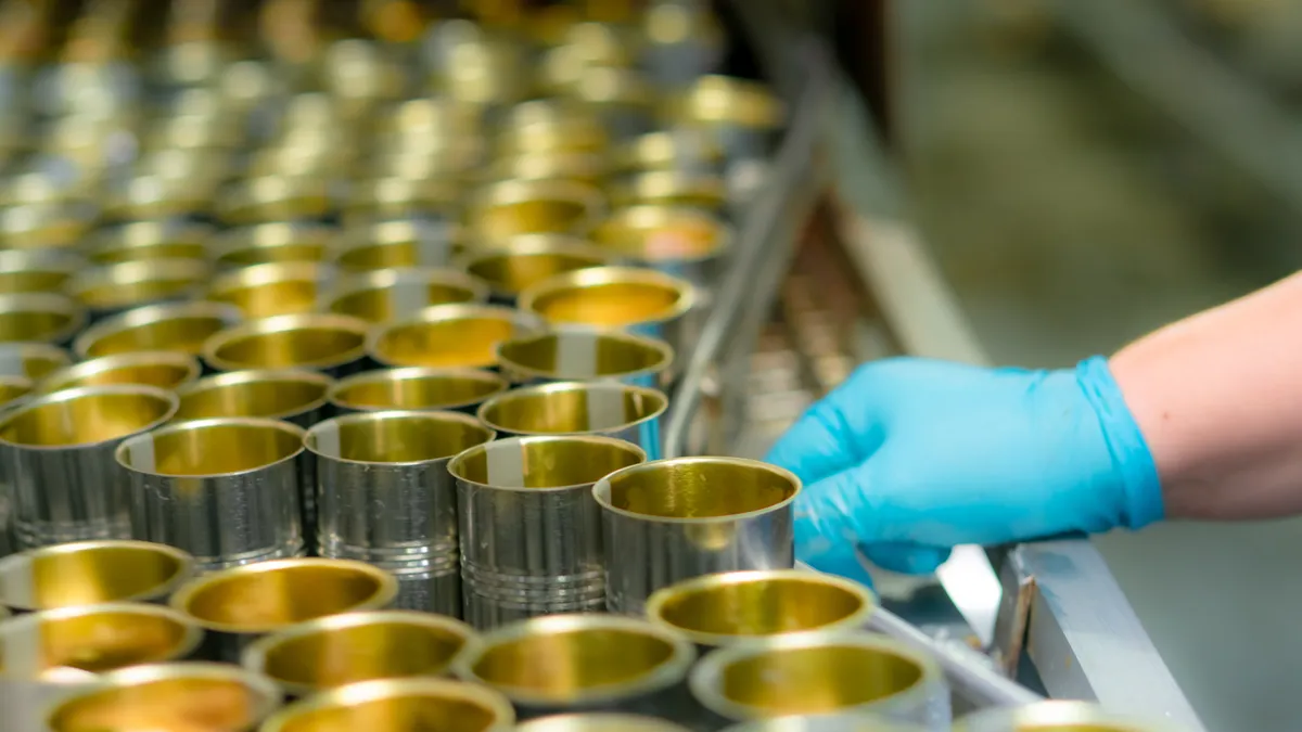 A person works on an assembly line to fill metal food packaging cans