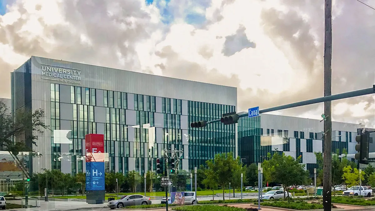 Street view of a tall, blocky silver building with many windows.