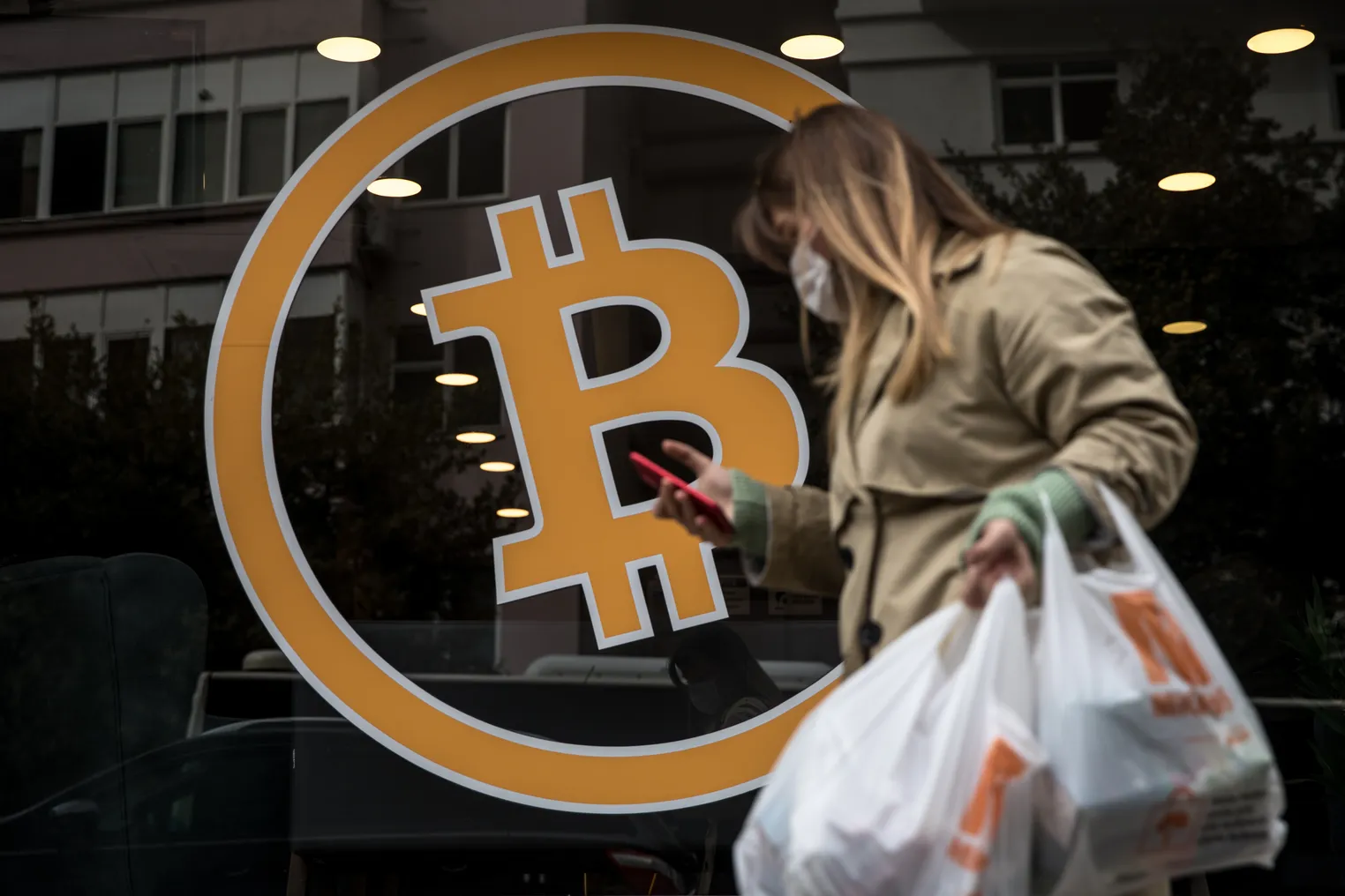 Person with shopping bag passes storefront window with Bitcoin sign