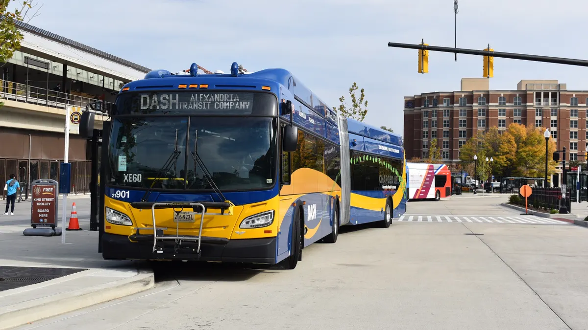 A blue and yellow bus lettered "100% Electric" and "DASH" on a street with trees.