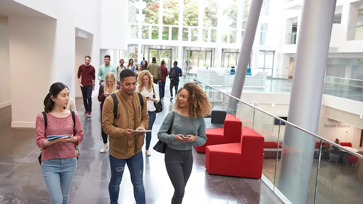 A diverse group of individuals walking through a spacious building, engaged in conversation and moving with purpose.