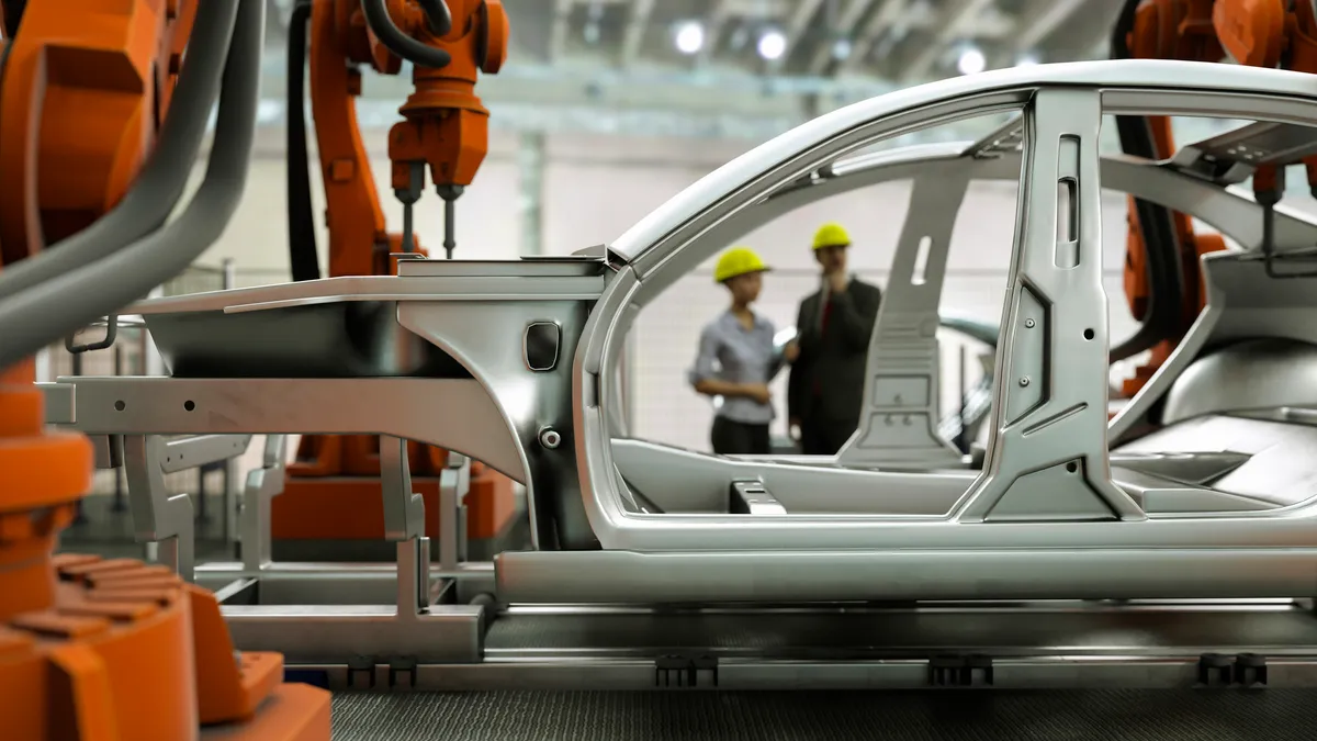 Modern car production line with robotic arms welding components 3D render and two workers with yellow helmets blurred in the background.