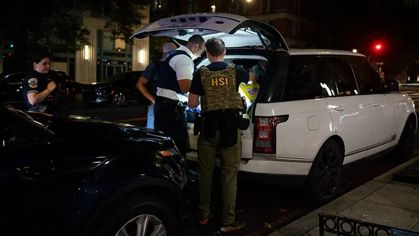 Federal agents inspecting a car's open trunk.