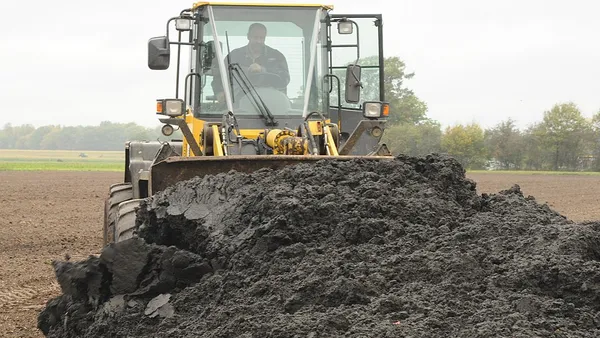 A farmer in a tractor is seen moving sewage sludge