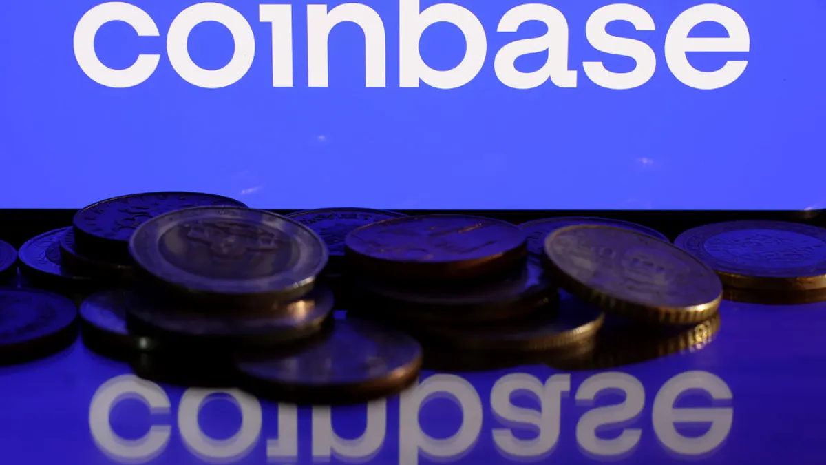 The Coinbase logo is shown on a blue screen. In the foreground, stacks of coins are piled up.