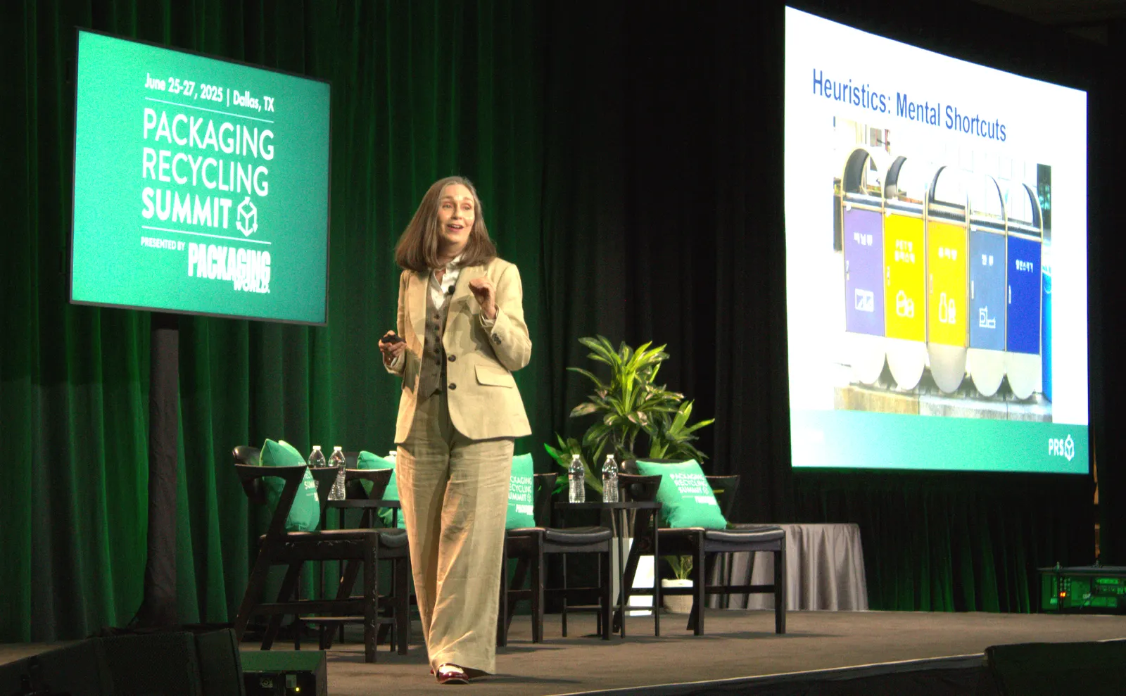 A person stands on stage in front of a green background that says Packaging Recycling Summit and addresses an audience.