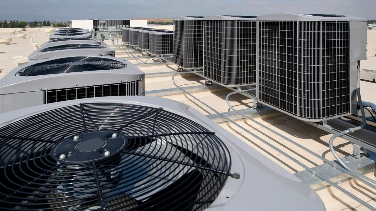 Two rows of air conditioning condensers are pictured on the roof of a large building.