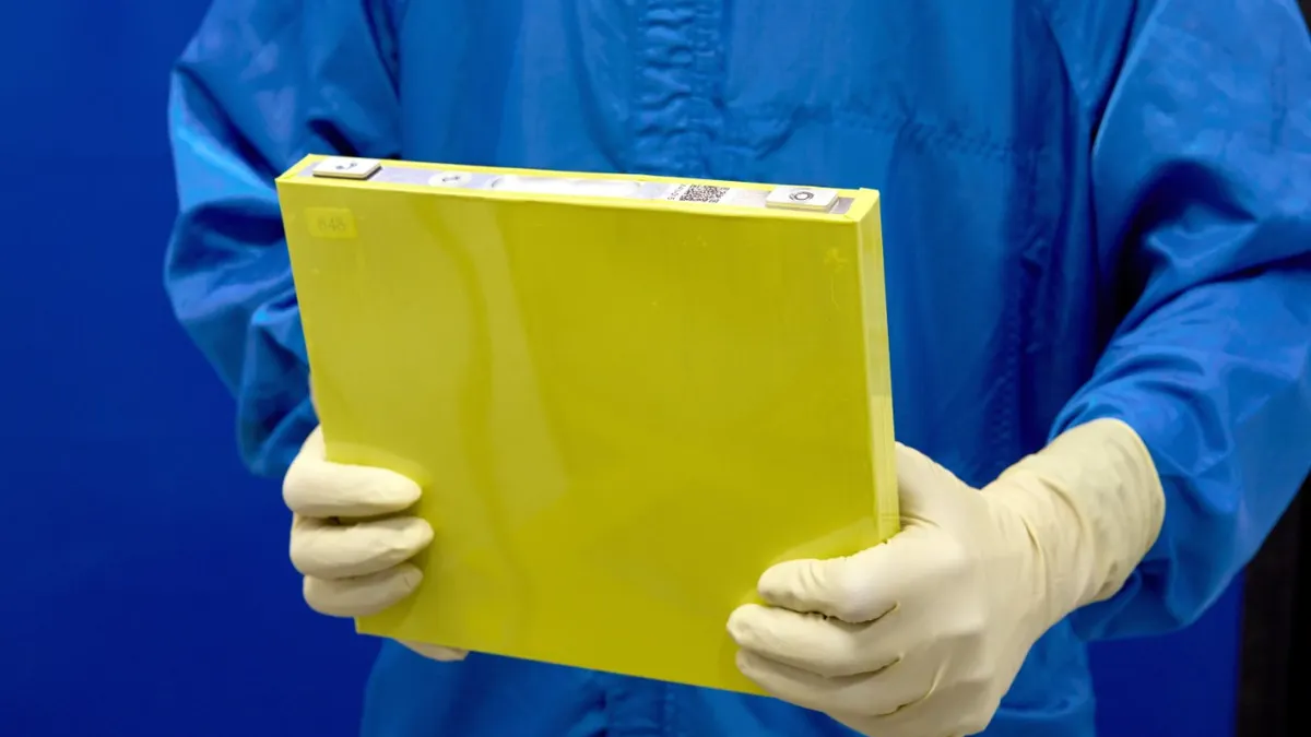 An employee wearing a blue protective suit holds a prototype LMR battery cell with a yellow housing at the General Motors Wallace Battery Cell Innovation Center in Warren, Michigan.
