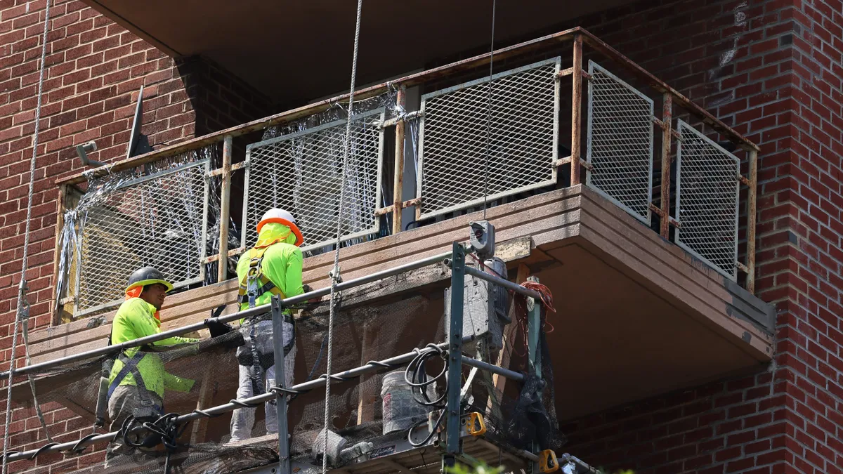 Two construction workers on a lift work on the exterior of a building.