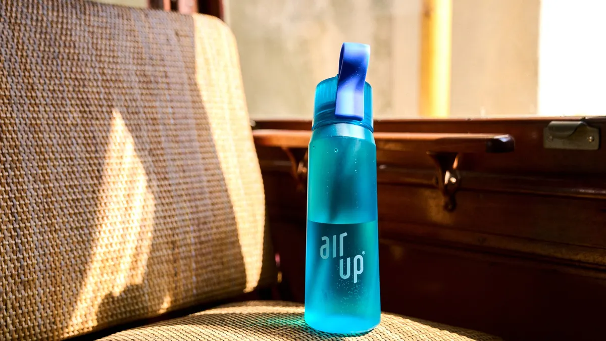 A blue Air Up water bottle sits on a brown seat next to a window.