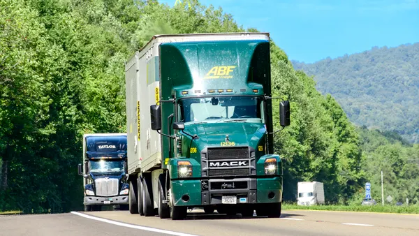 Trucks on an interstate with trees along hillsides in the background.