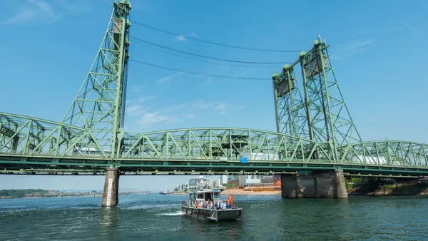 A boat passes under a green lift bridge.