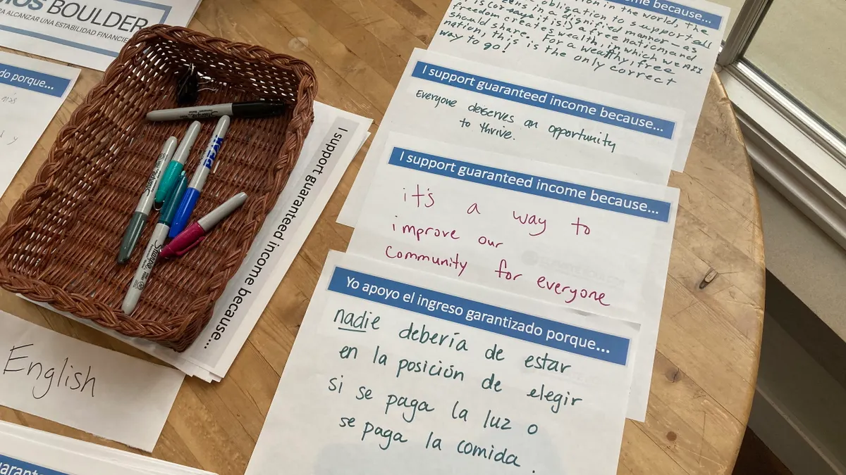 Sheets of paper on a table that say "I support guaranteed income because...." with written statements on them in English and Spanish.