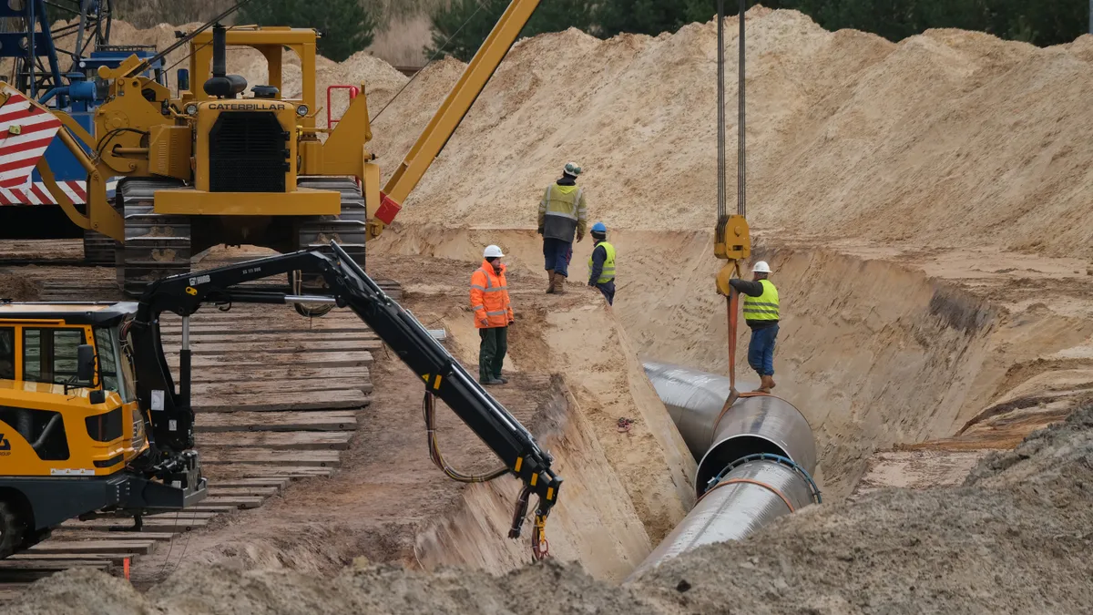 Construction workers stand around a pipeline project.