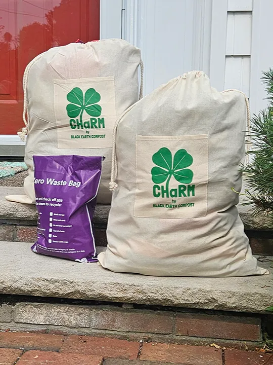 Two woven sacks with a &quot;CHaRM by Black Earth Compost&quot; logo sit next to a plastic bag labeled &quot;Zero Waste Bag&quot; on the front steps of a house.