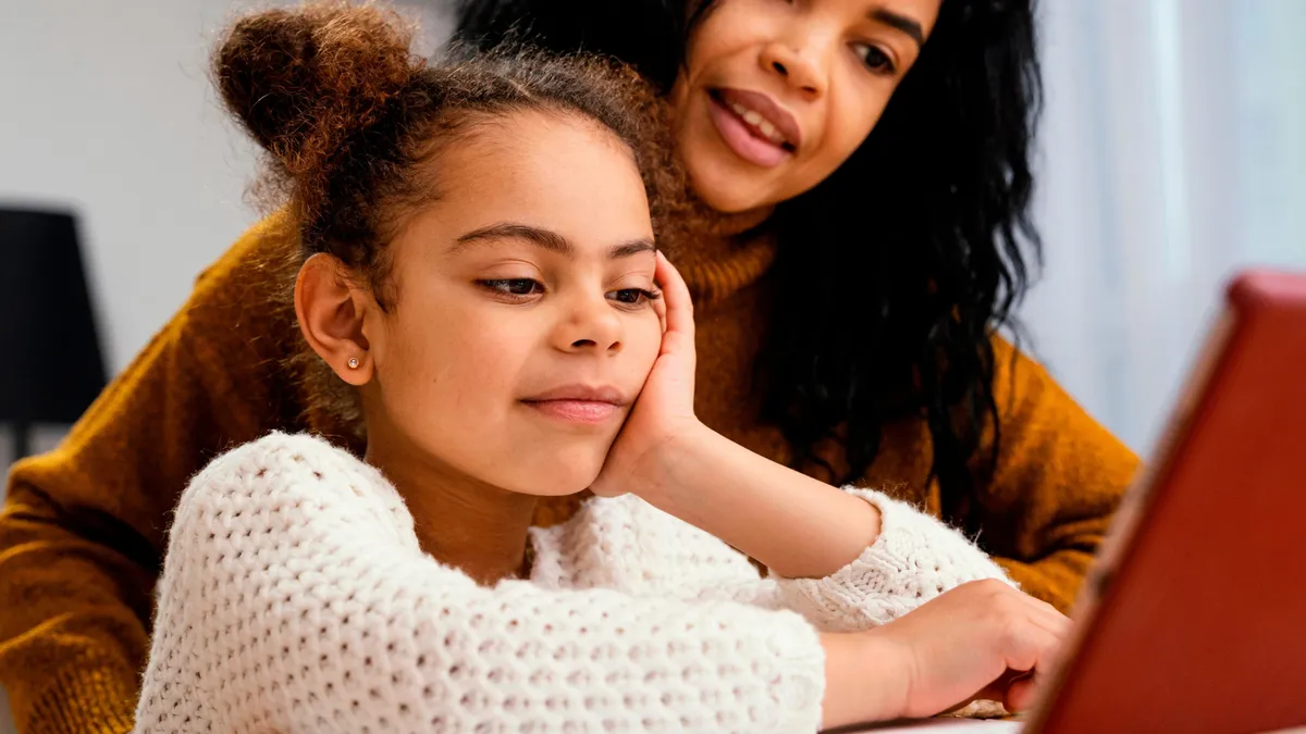 Smiling teenager helping younger sibling during online school with tablet