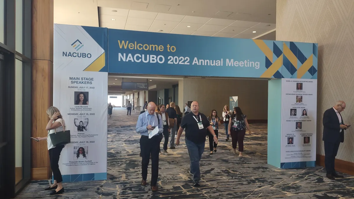 People walk under a sign marking the NACUBO 2022 Annual Meeting.