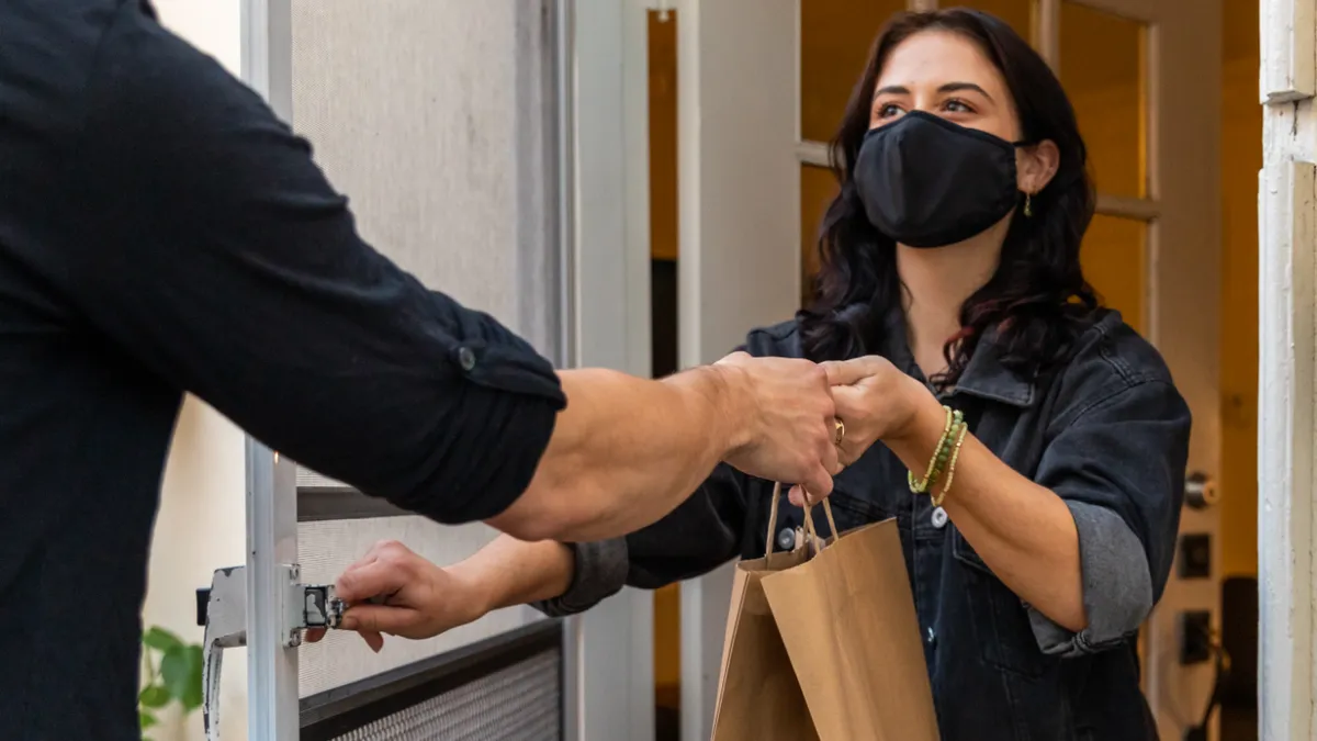 A masked woman is delivered groceries in a paper bag.