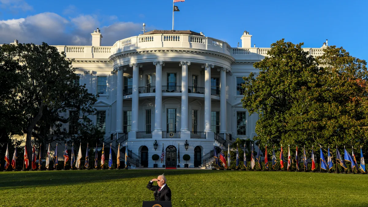 The president joe biden stands behind a podium in front of the white house, shielding his eyes from the sun.