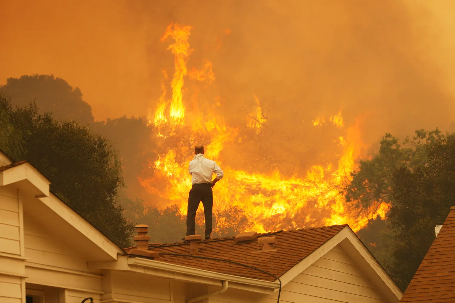 A man on a rooftop looks at approaching flames.