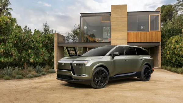 The 2027 Lexus TZ electric SUV parked outdoors in front of a modern home with glass walls.