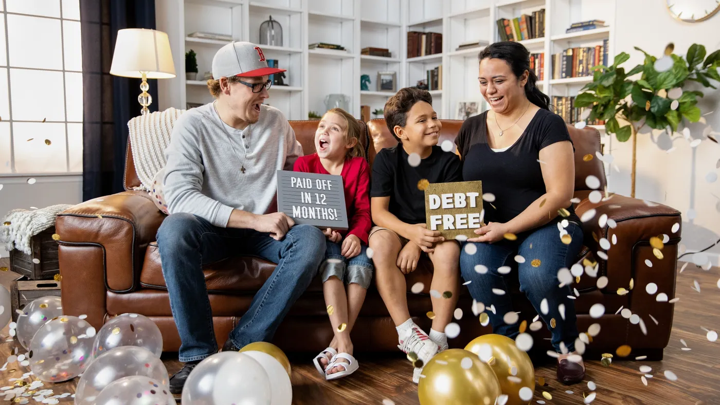 A family celebrates paying off something large and are holding cards expressing they are free of debt.