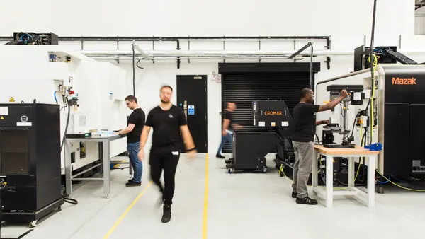 Workers operate machinery in a bright, modern manufacturing facility with high-tech equipment.