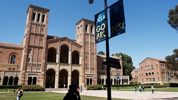 People walking along campus street, with a street and banner in foreground and brick buildings in background.