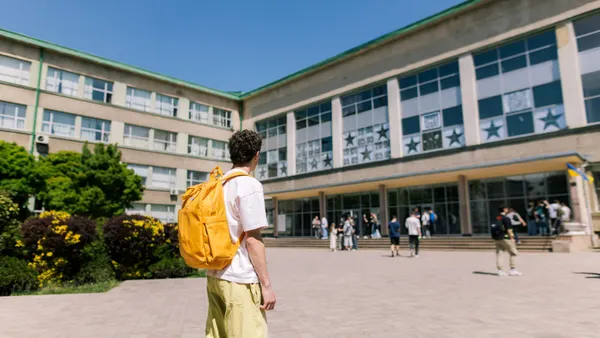 A student wearing a backpack gazes at a campus building.
