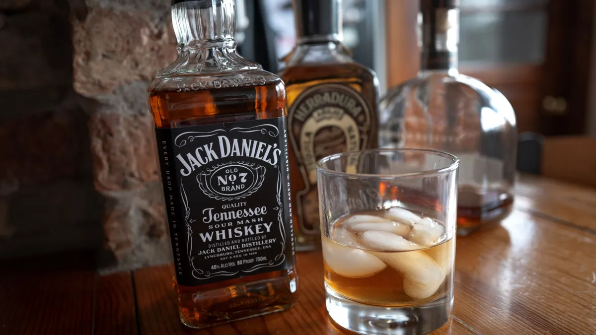 A glass of Jack Daniel's with ice is next to a bottle of it.