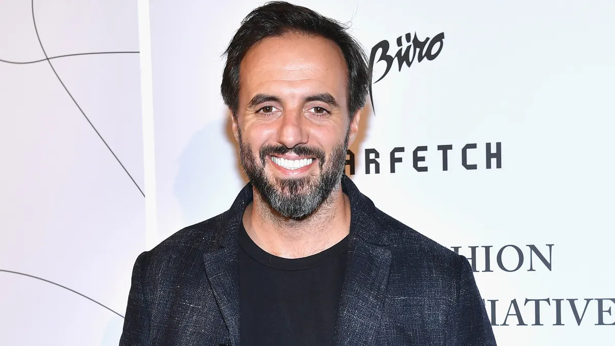 A man, José Neves, stands and smiles at the camera while wearing a black t-shirt under a blazer.