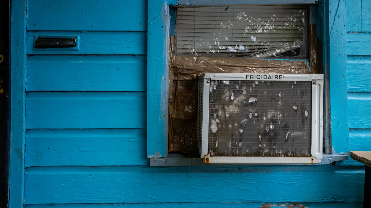 A window air conditioning unit in the window of a blue house.